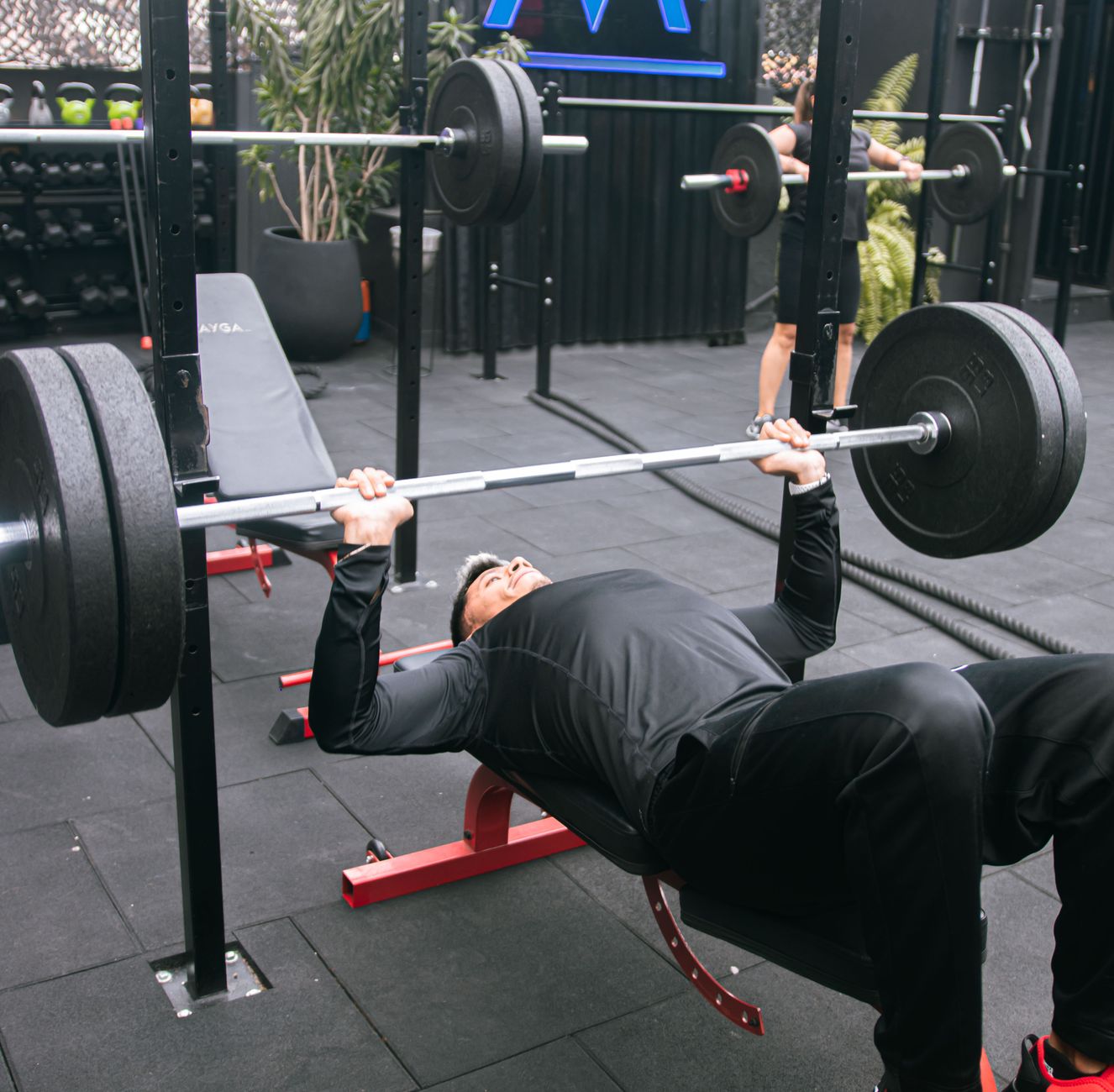Man performing a proper barbell bench press on a weight bench with safety spotter arms.