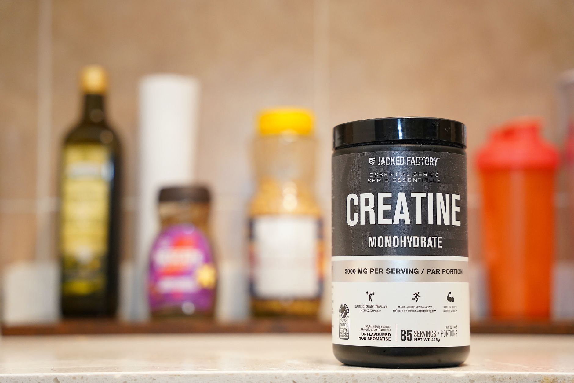 A person holding a tub of creatine powder in a gym setting.