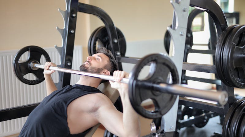 Man performing a barbell bench press with a spotter in a well-equipped gym, demonstrating a push day exercise.
